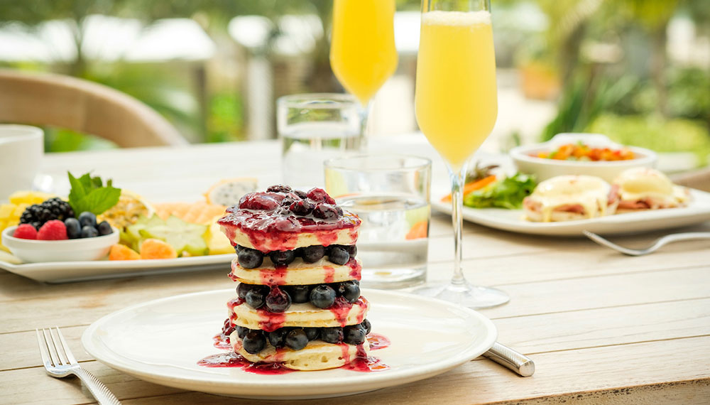 two mimosas at our outdoor seating table with a stack of pancakes in front and two other dishes in the background.