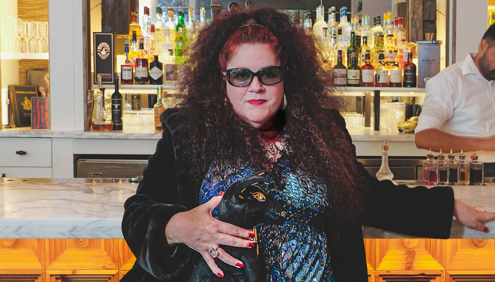 Wicki Wheaton, comedian, standing in front of a bar
