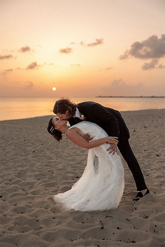 Newlyweds kiss on the beach at sunset